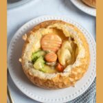 Pinterest graphic with text and photo of bread bowl full of cheesy vegetable chowder.