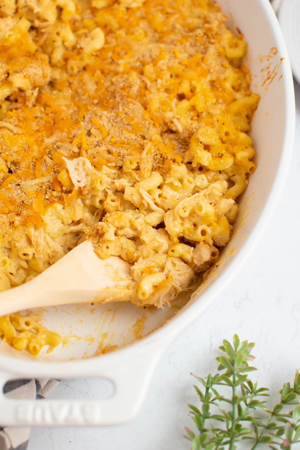 White baking dish with chicken and macaroni casserole and wooden spoon.