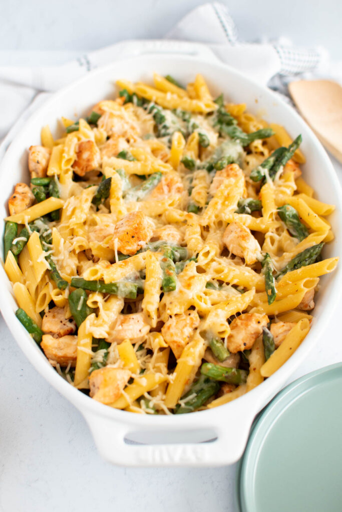 White dish full of chicken, asparagus, and pasta covered with parmesan cheese.