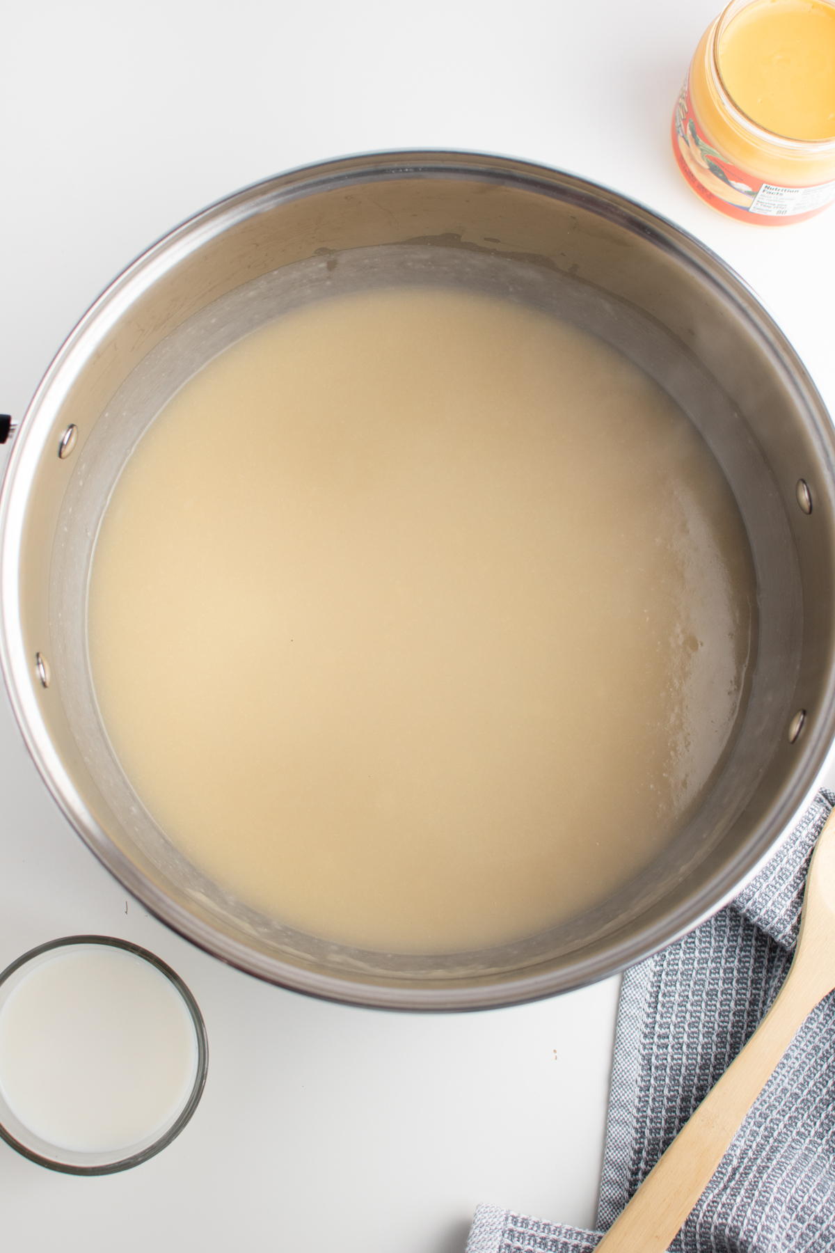 Chicken broth mixed with roux in large metal cooking pot next to wooden spoon.