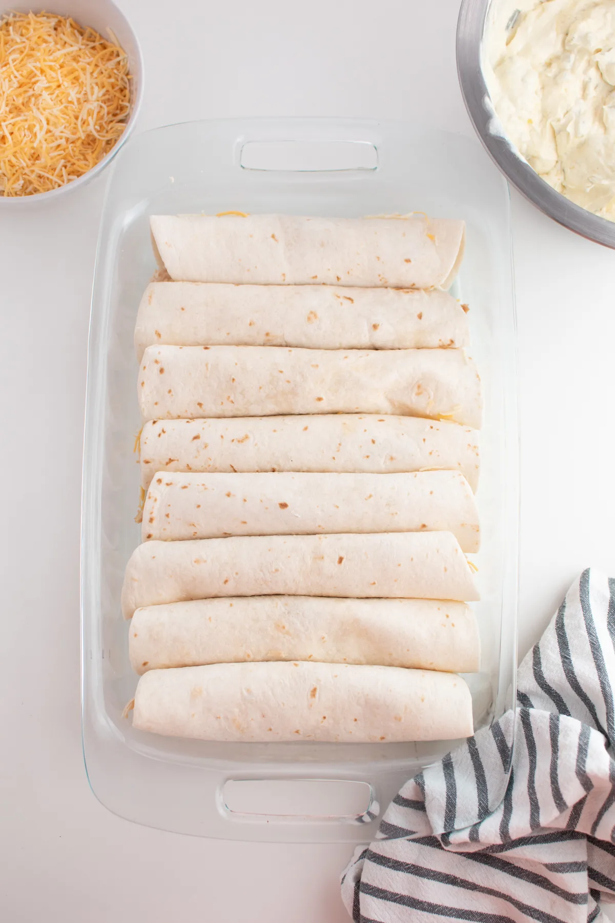Several chicken enchiladas lined up in clear glass baking dish with no sauce.