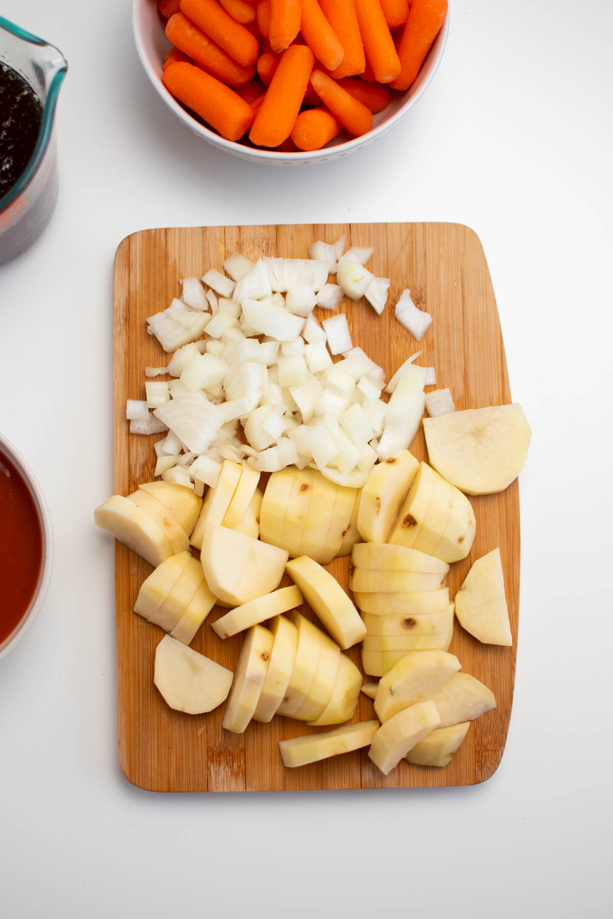 Chopped onion and potato slices on wood cutting board all on white table.