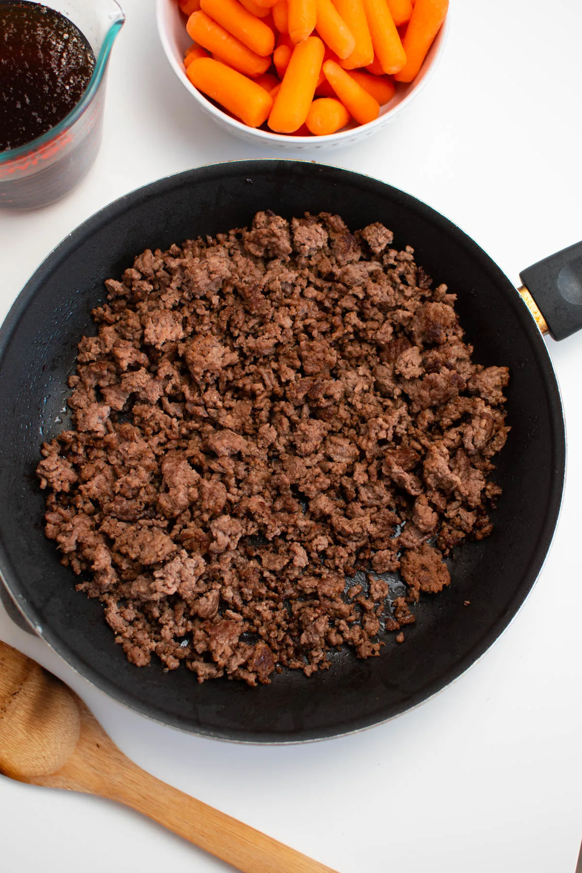 Cooked ground beef in black frying pan on white table.