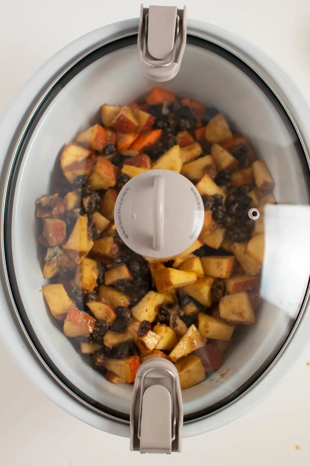 Lid on slow cooker full of sweet potatoes, apples, and dried cranberries.