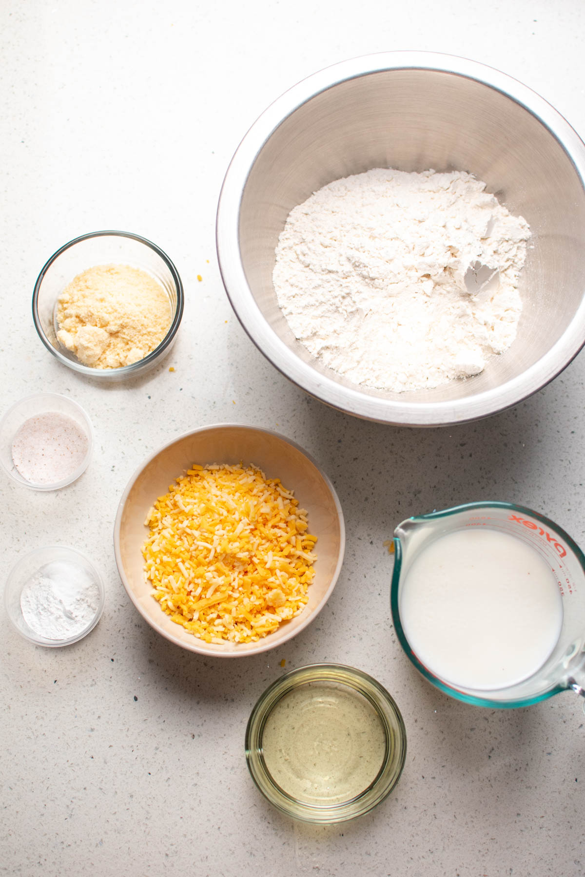 Bowls of ingredients for parmesan drop biscuits including flour, cheese, and milk.