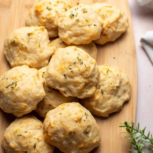Parmesan drop biscuits arranged on wood cutting board with greenery stem nearby.