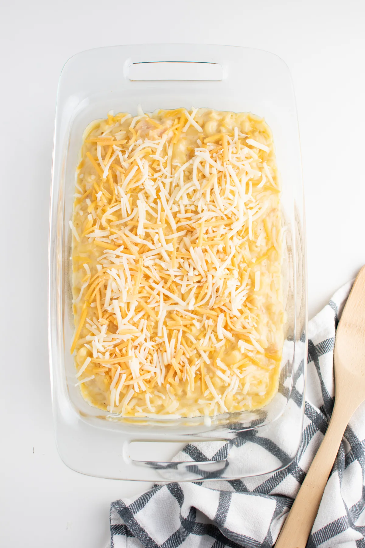 Shredded cheese on top of baked macaroni in clear casserole baking dish.