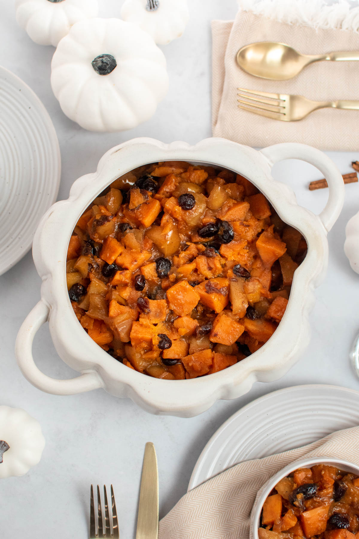 Slow cooker sweet potatoes in white pumpkin dish on table with place settings and white pumpkins.