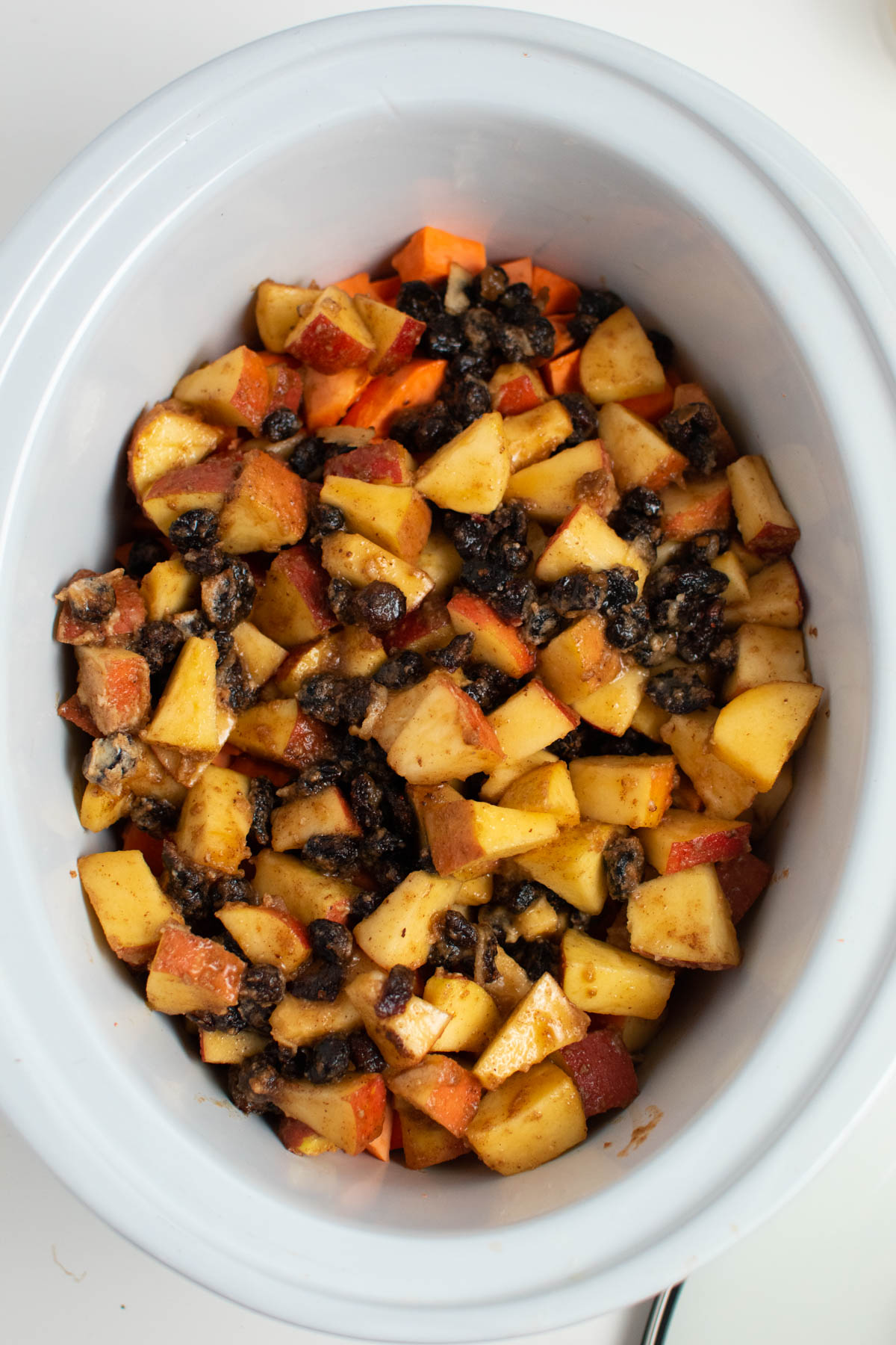 Sweet potatoes and apples in slow cooker insert on white table.