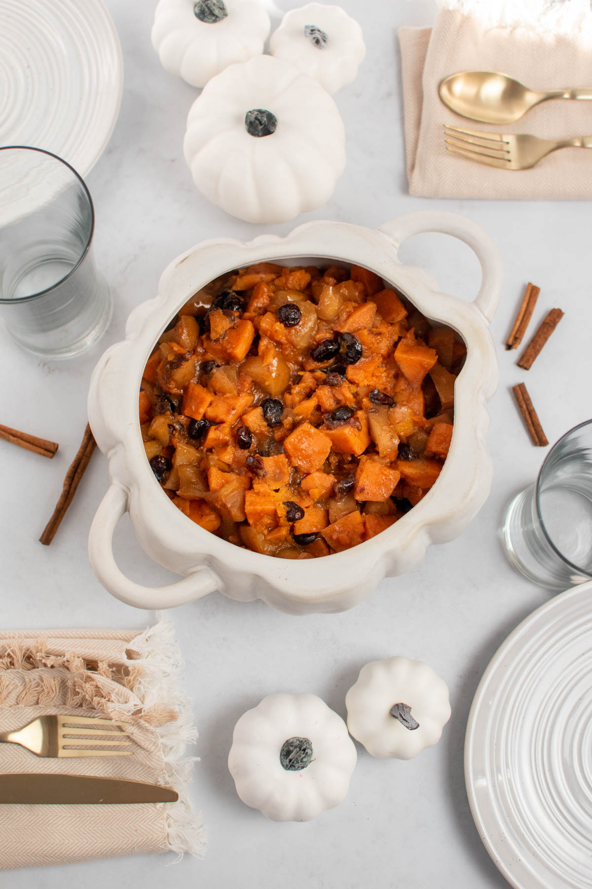 Crock Pot sweet potatoes in white pumpkin dish on table with place settings and white pumpkin decor.