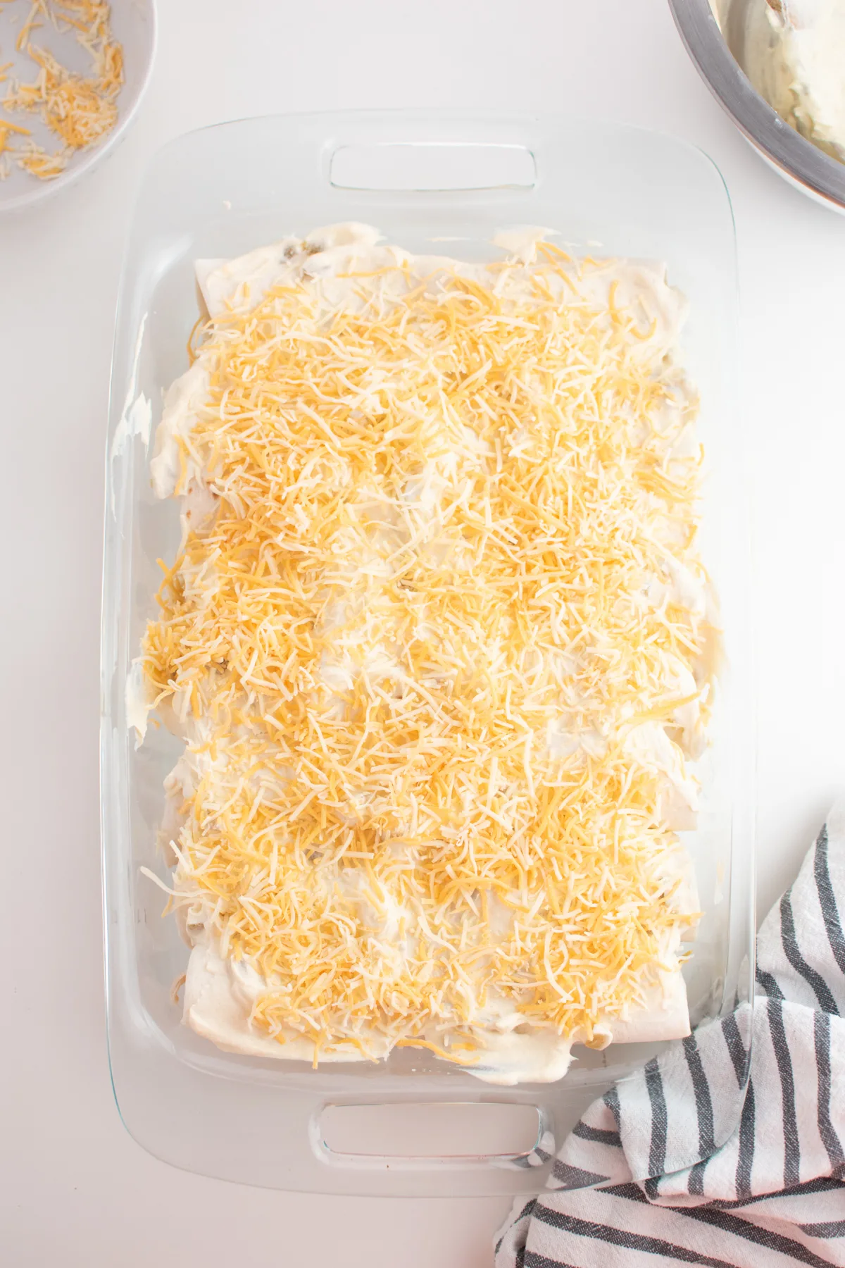 White chicken enchiladas lined up in clear glass dish with shredded cheese.