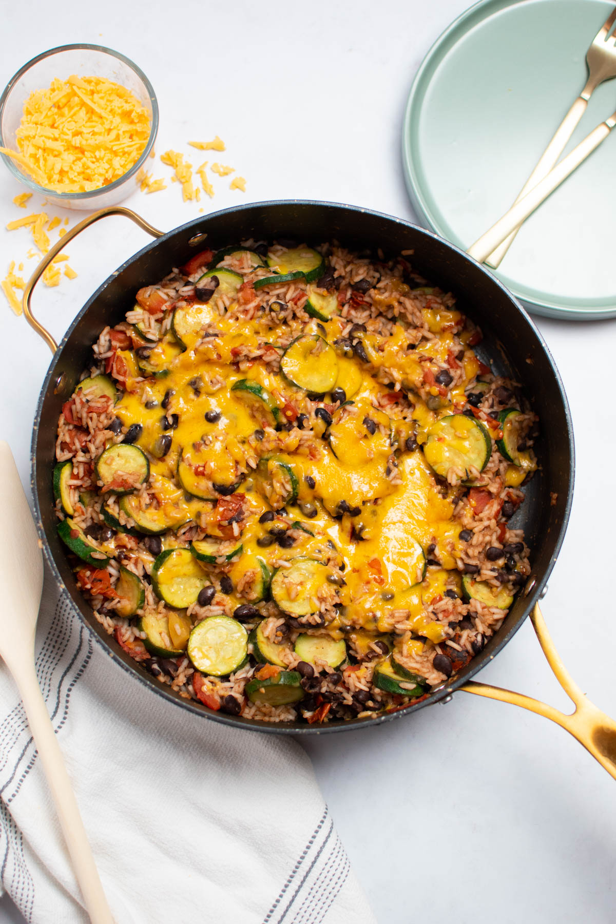 Zucchini, black bean, and rice dinner in large black skillet with plates and a towel nearby.