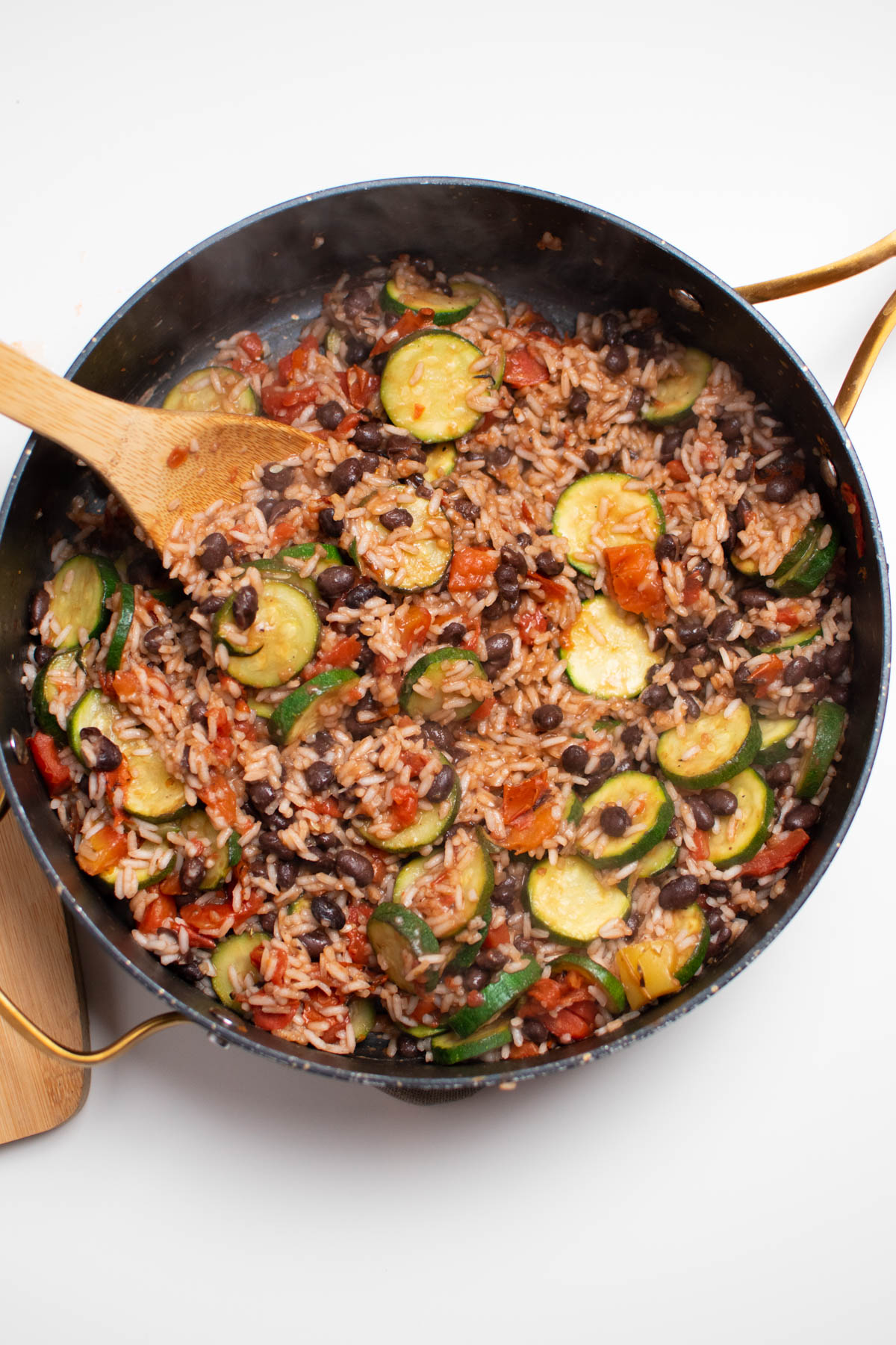 Zucchini, black beans, rice, and tomatoes in large black skillet with wooden spoon.