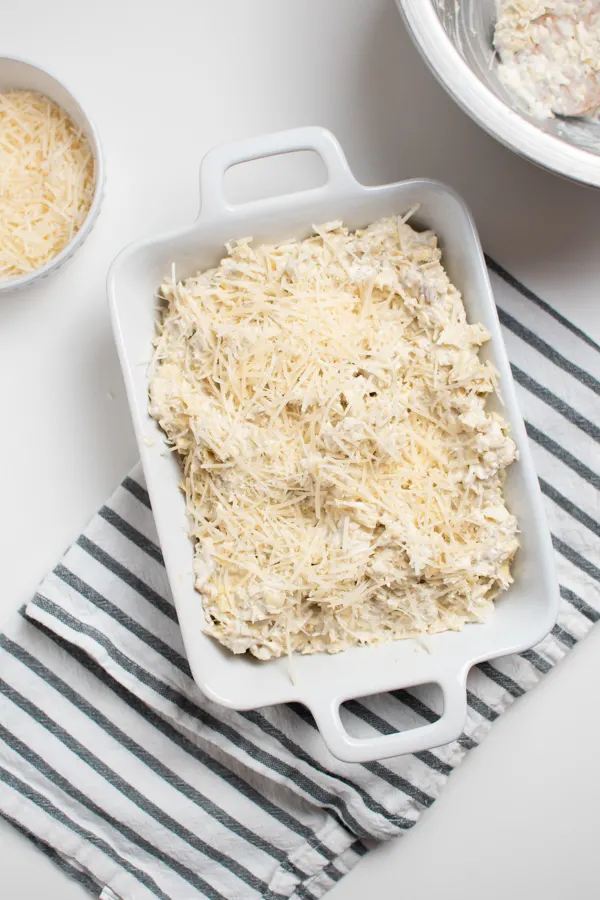Artichoke dip recipe in small white casserole baking dish topped with cheese.