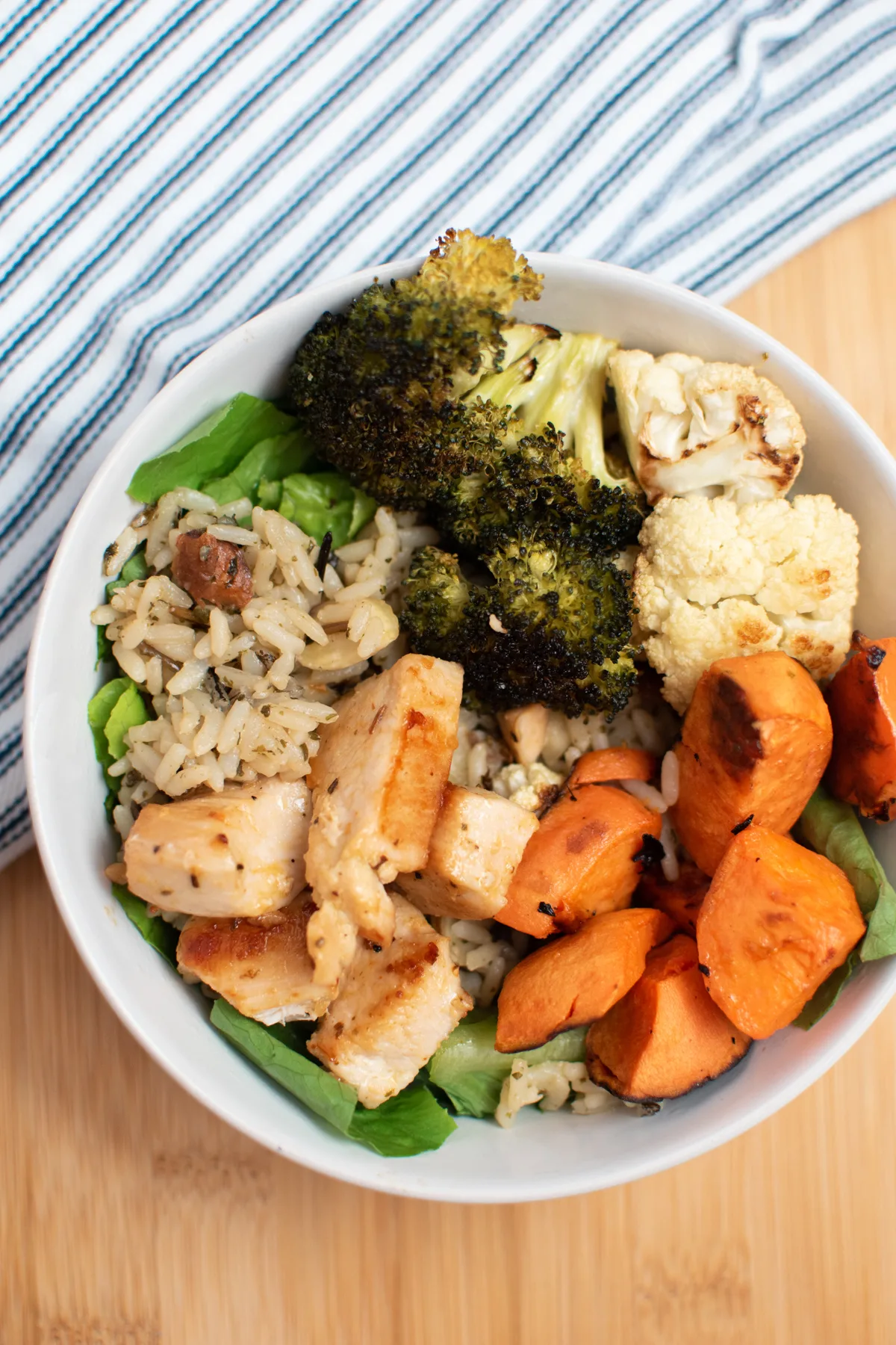 A chicken power bowl on a cutting board topped with sweet potatoes, lettuce and broccoli.