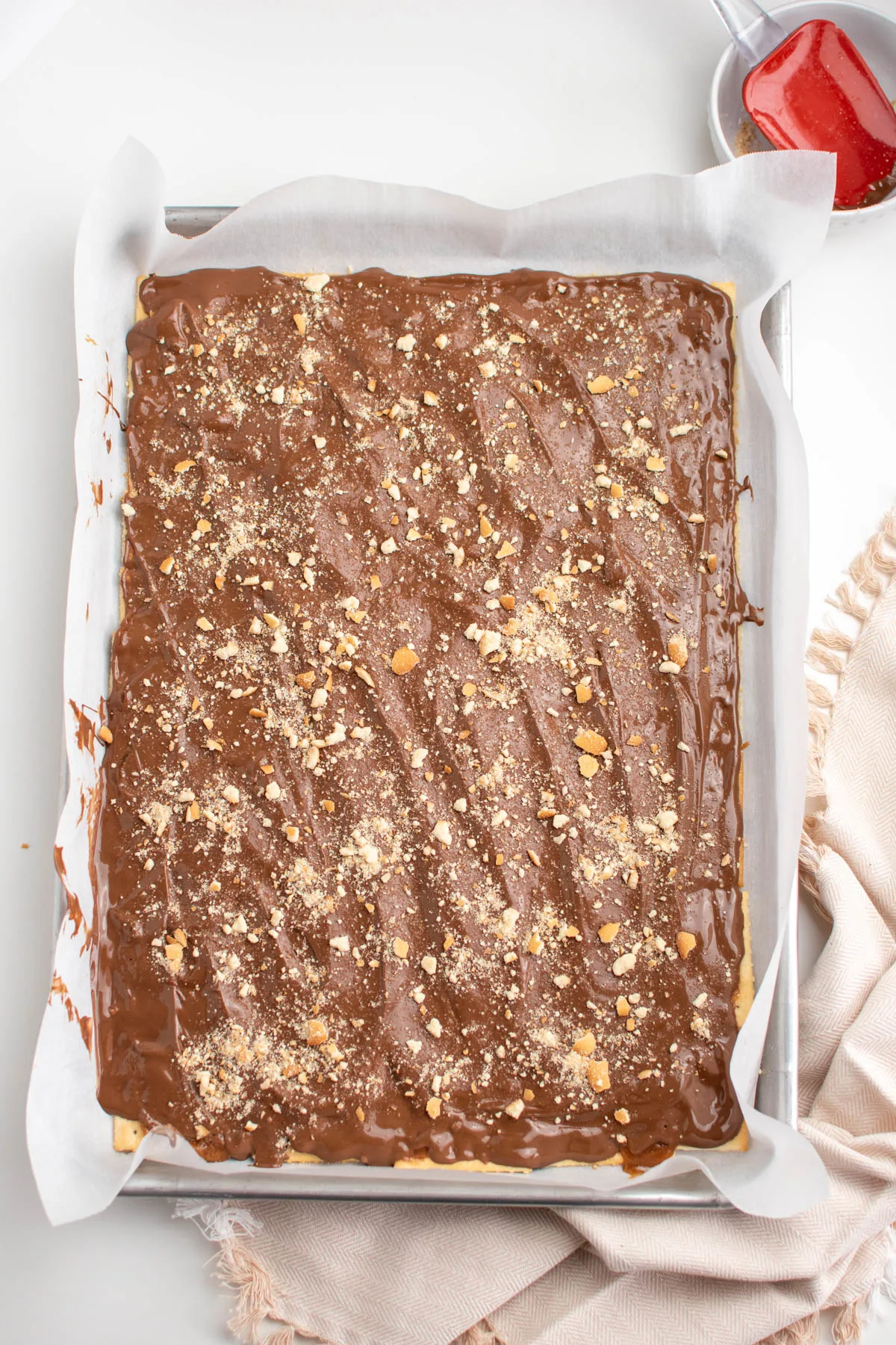 Cracker candy with crumb topping on parchment paper lined baking sheet next to kitchen towel.