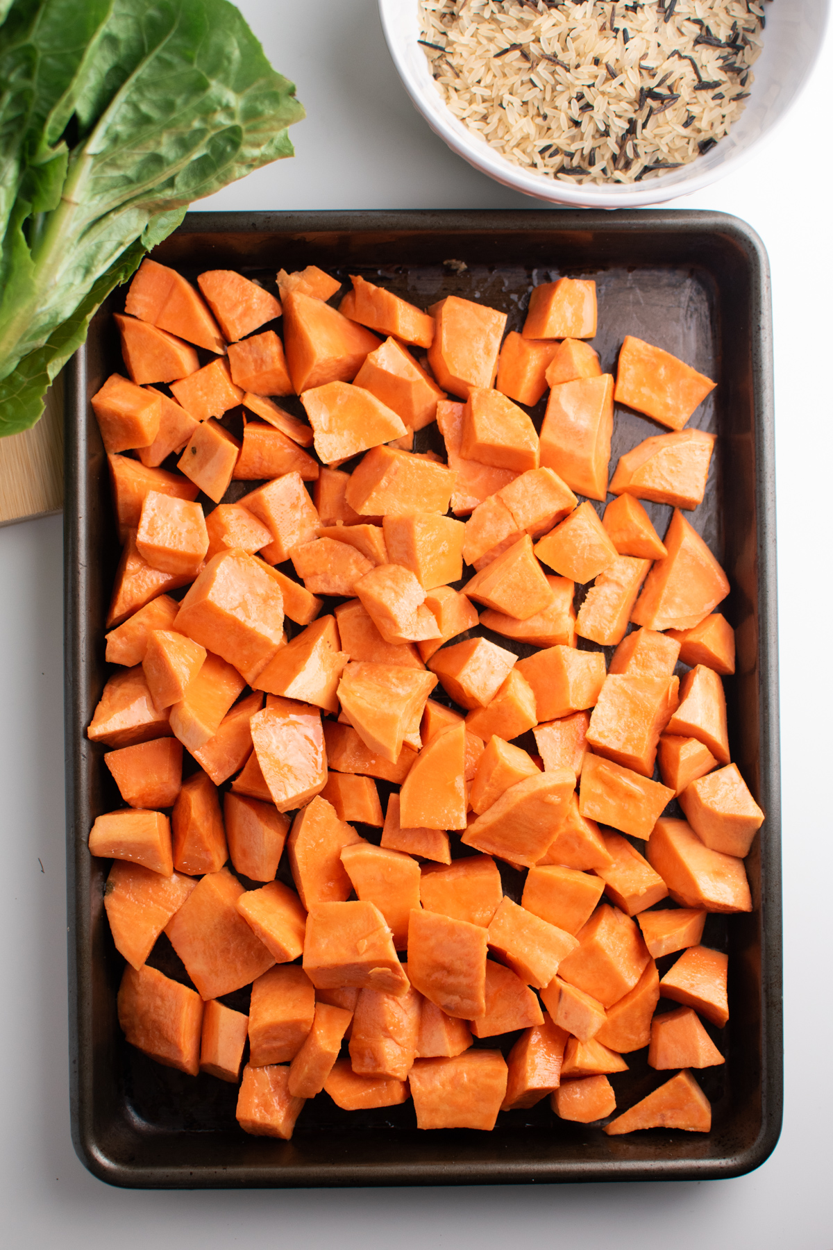 Cubed sweet potato pieces on sheet pan next to lettuce and wild rice.