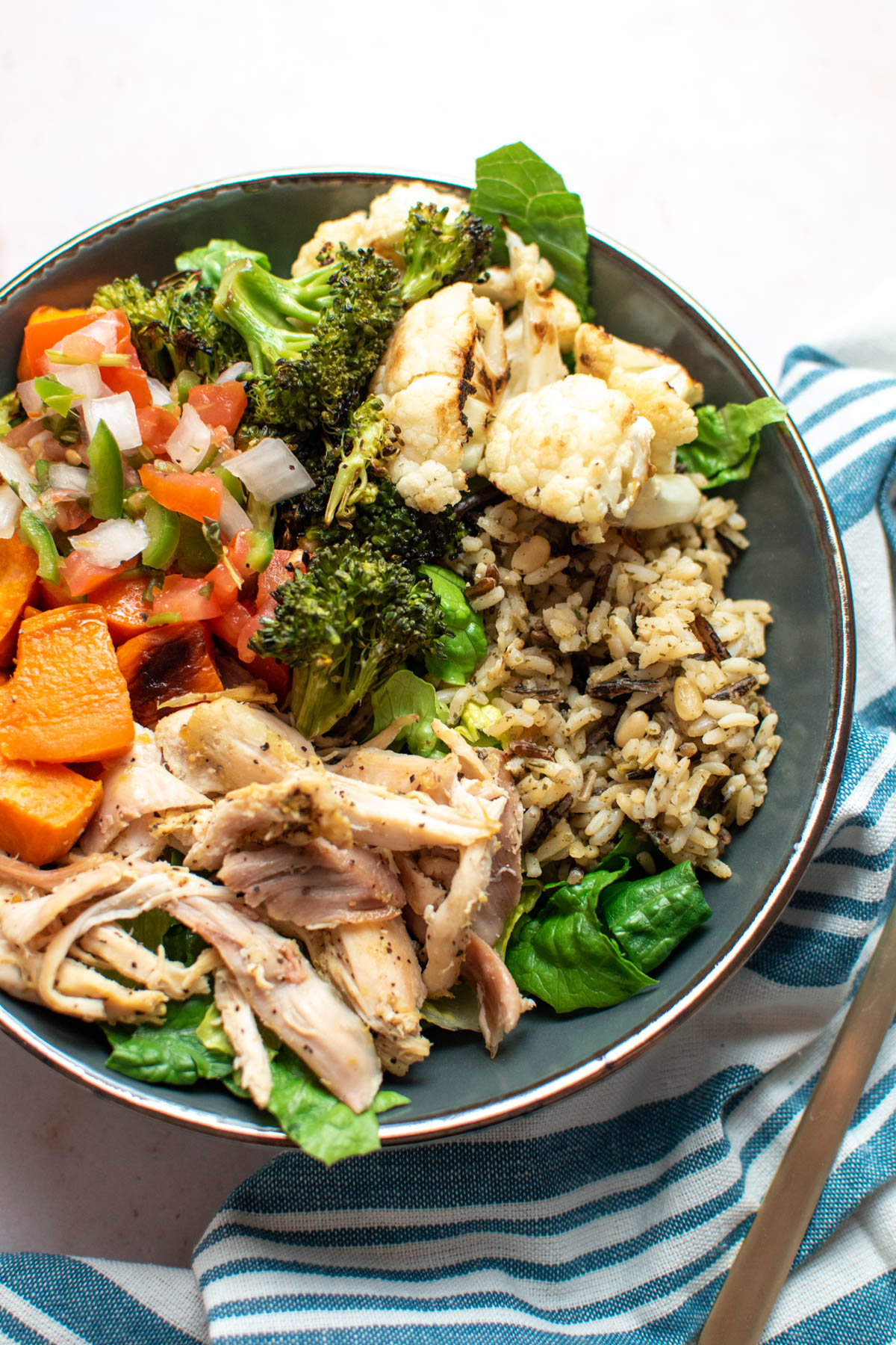 Chicken power bowl with roasted cauliflower, broccoli, and sweet potatoes on table.