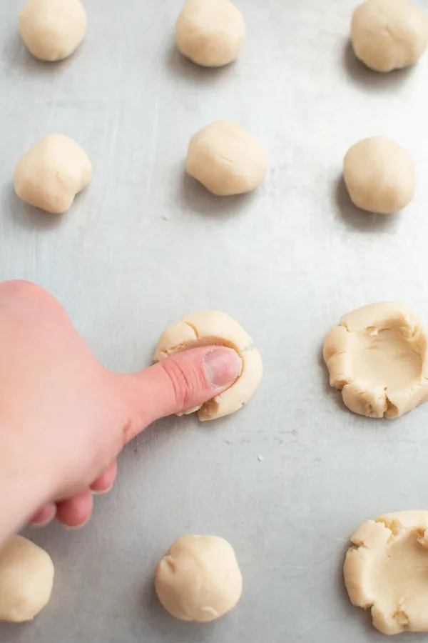 Woman makes easy thumbprint cookies by smashing down small balls of dough.