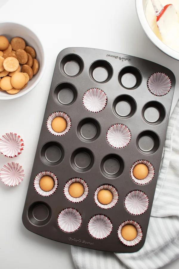 Vanilla wafers inside mini cupcake liners in mini muffin tin next to bowl of wafers.