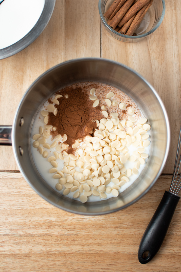 Overhead view of white chocolate chips, cinnamon, and milk in a sauce pan.