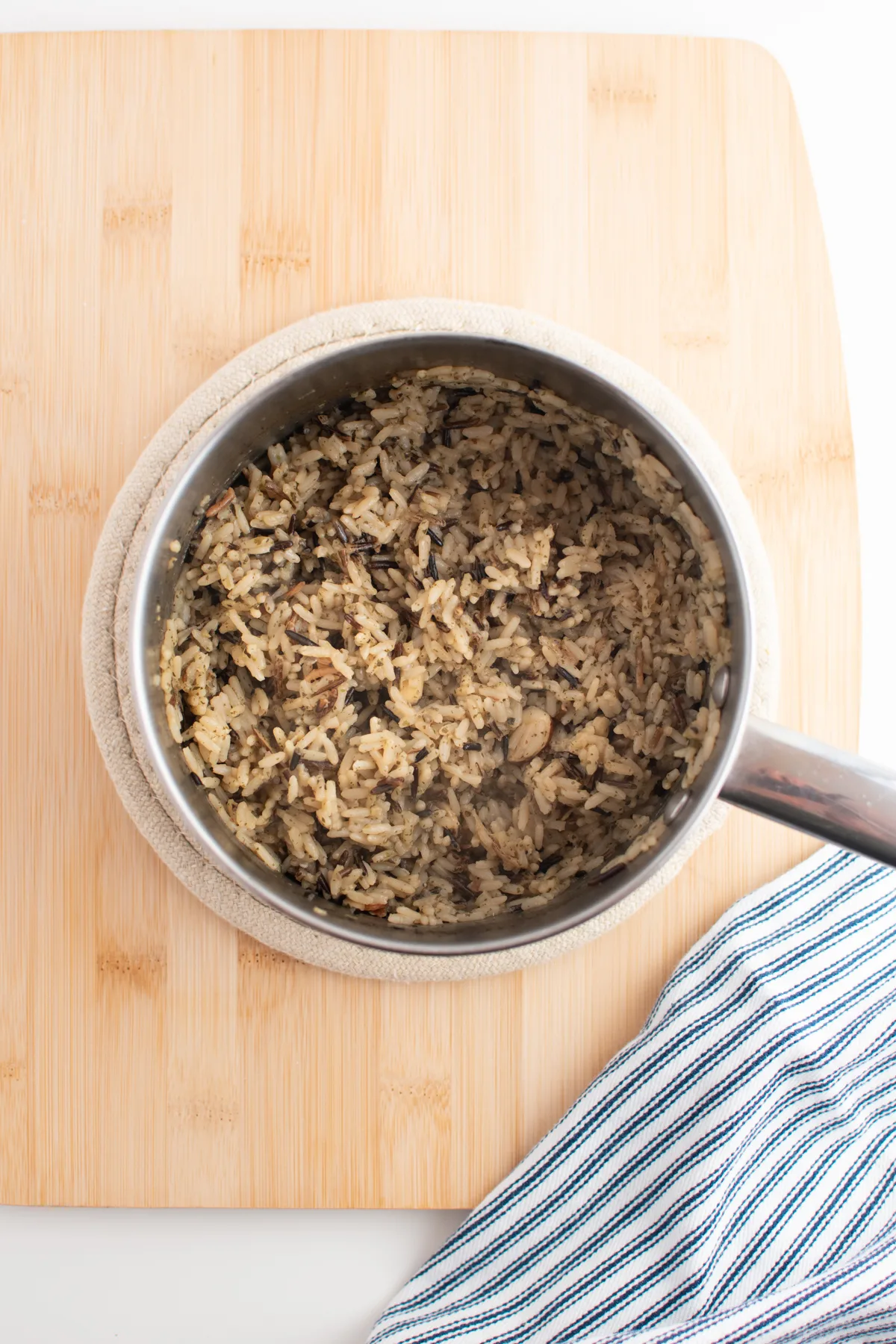 Wild rice in small metal stock pot next to blue and white striped kitchen towel.