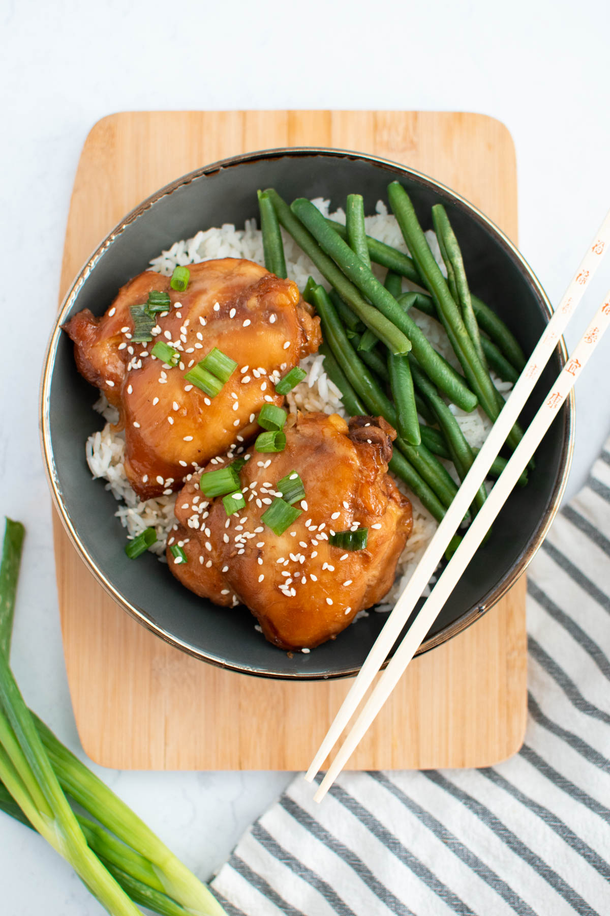 Asian chicken thighs with rice, green, beans, and sesame seeds in bowl with chop sticks.