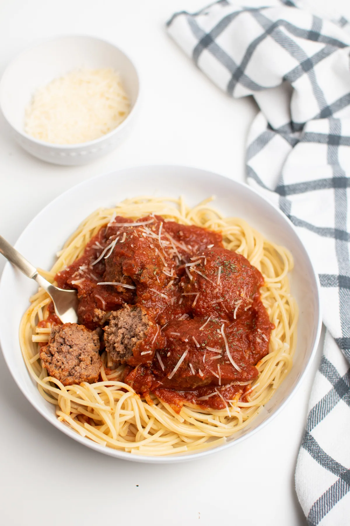 Authentic spaghetti and meatballs and gold fork in white bowl on white table.