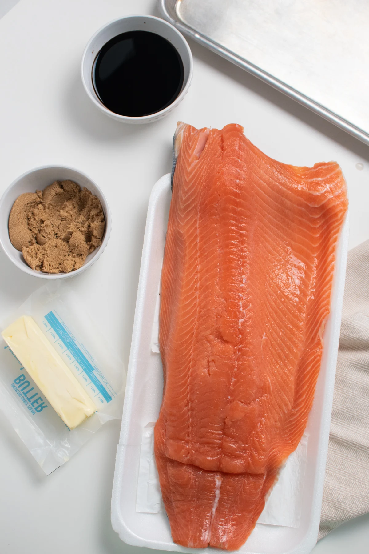 Baked salmon ingredients on white table including salmon, brown sugar and butter.