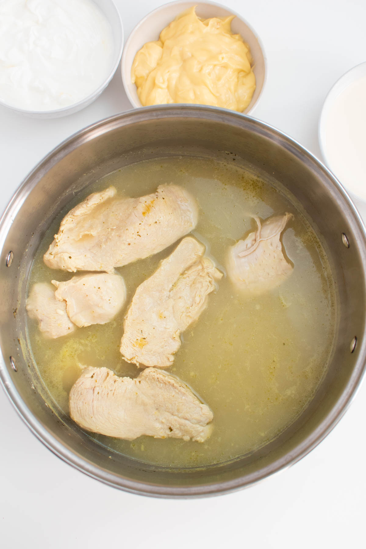 Several boiled chicken pieces in large pot of broth on white table.