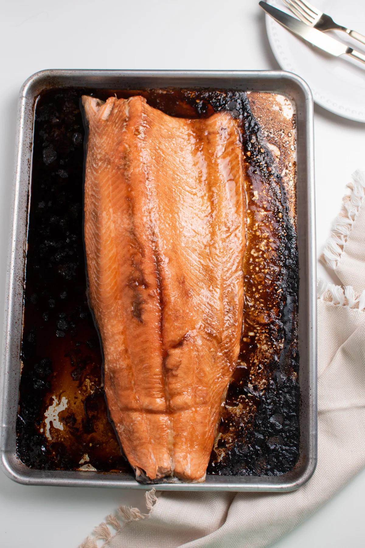 Cooked brown sugar salmon fillet on a baking sheet next to cream colored kitchen towel.