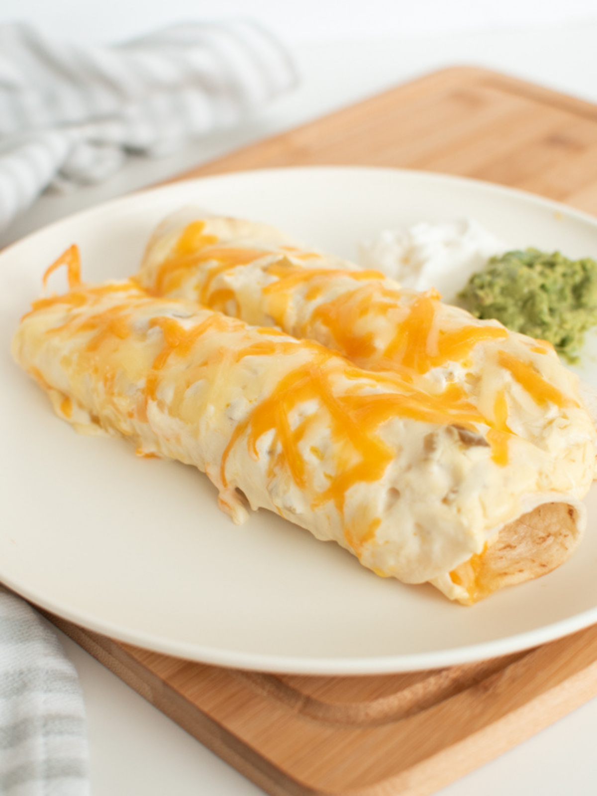 Chicken enchiladas with sour cream white sauce and guacamole on white plate.