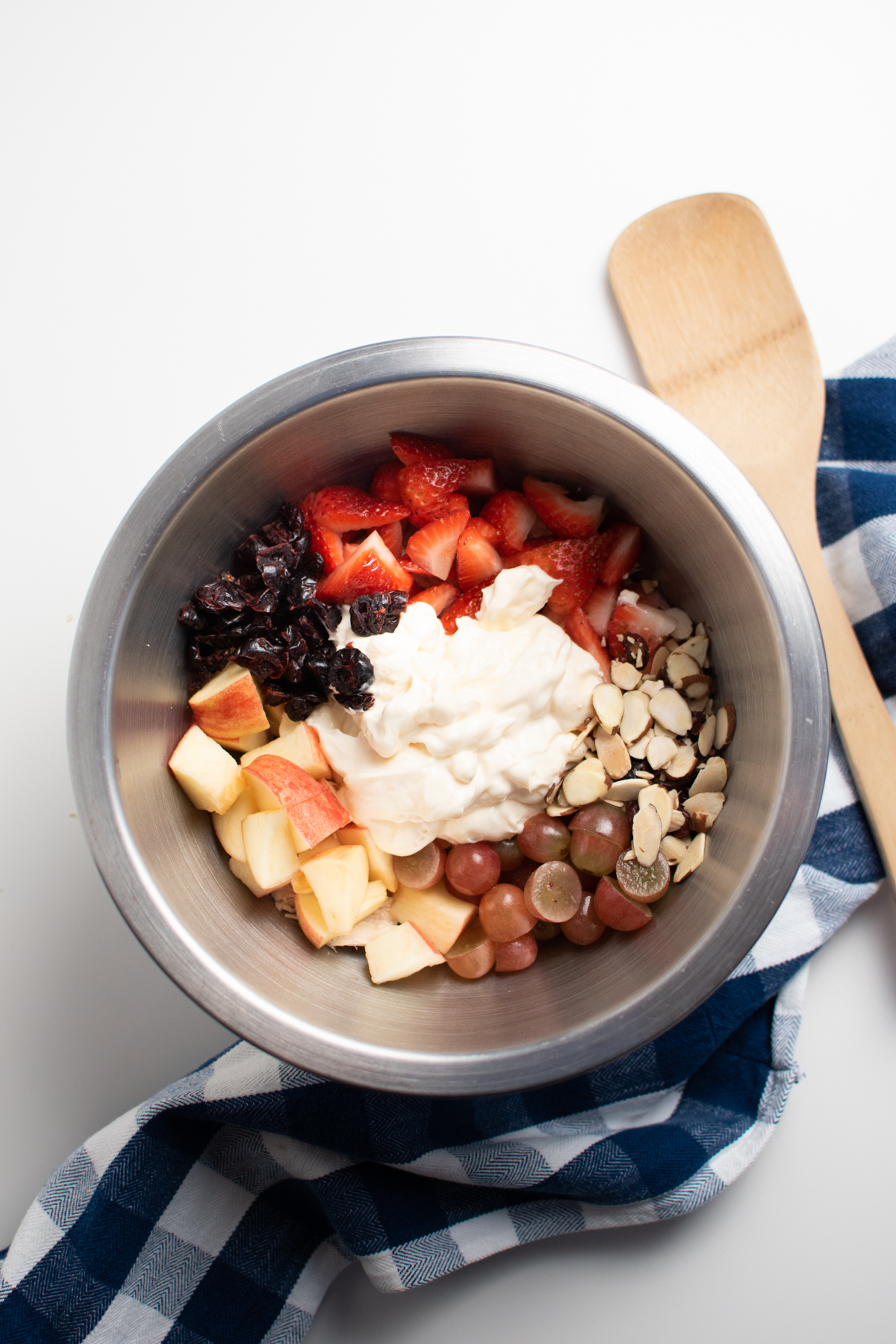Mayonnaise, apples, strawberries, grapes, almonds, and dried cranberries in metal mixing bowl.