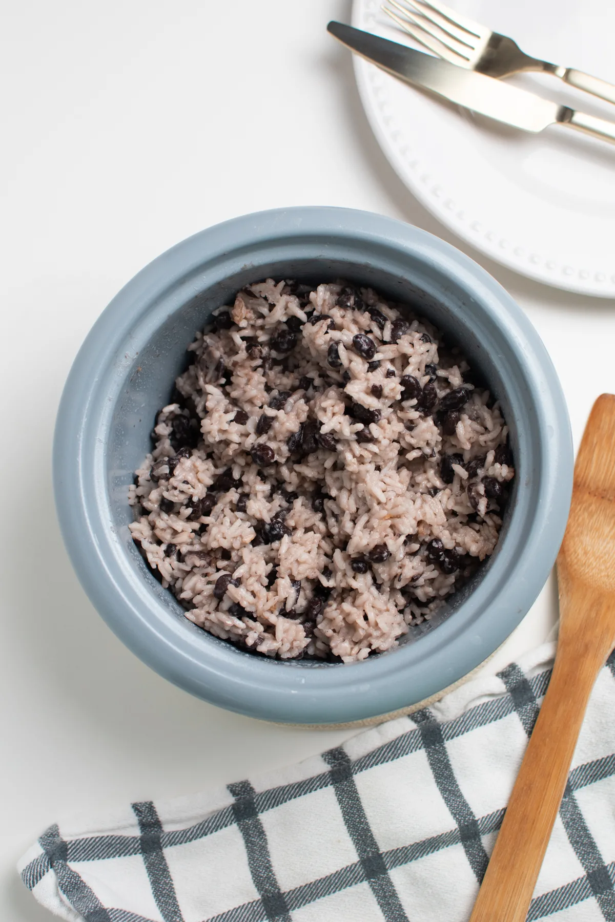 Coconut rice with black beans in rice cooker with blue rim and kitchen towel.