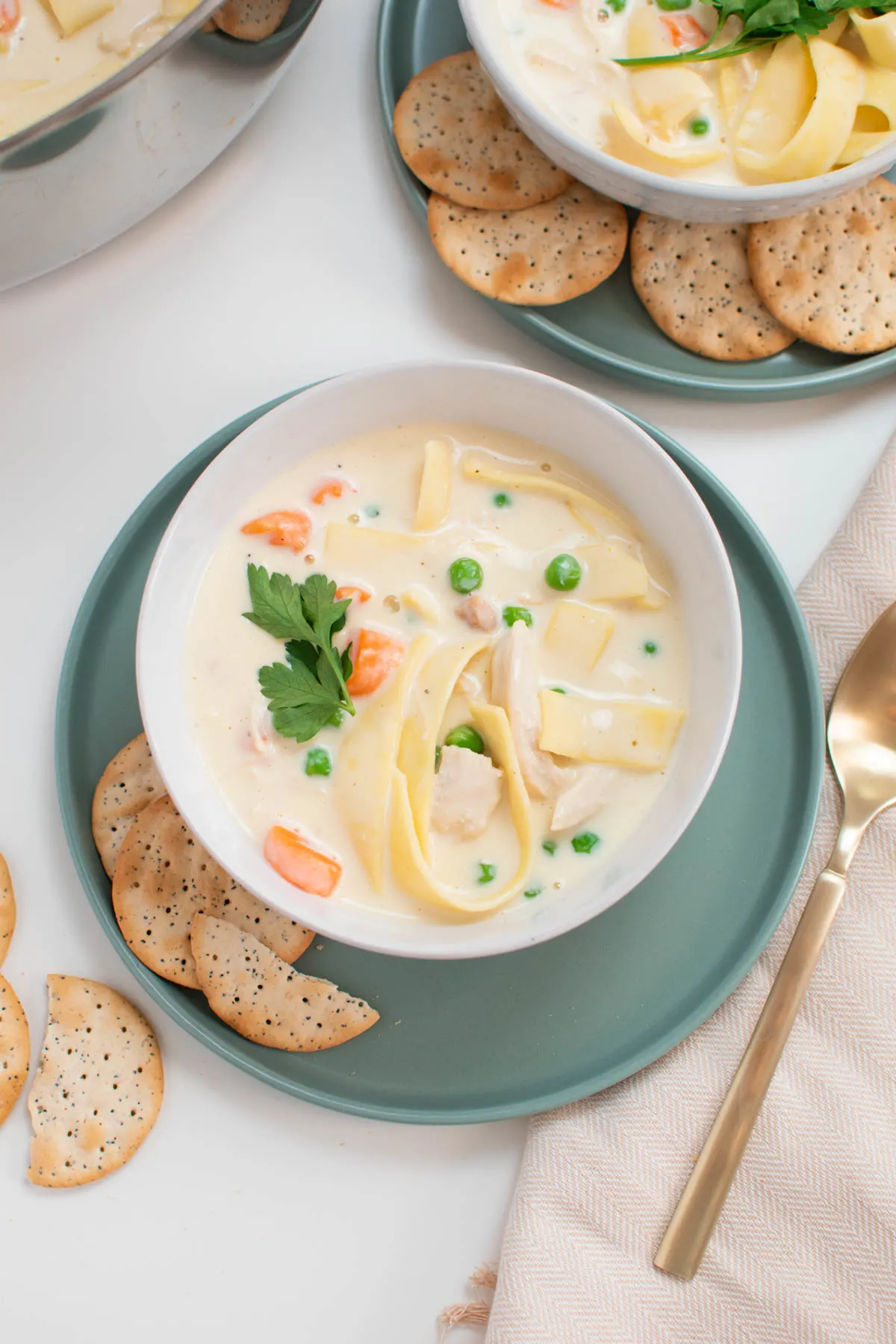 Bowl of creamy chicken noodle soup on green plate with crackers.