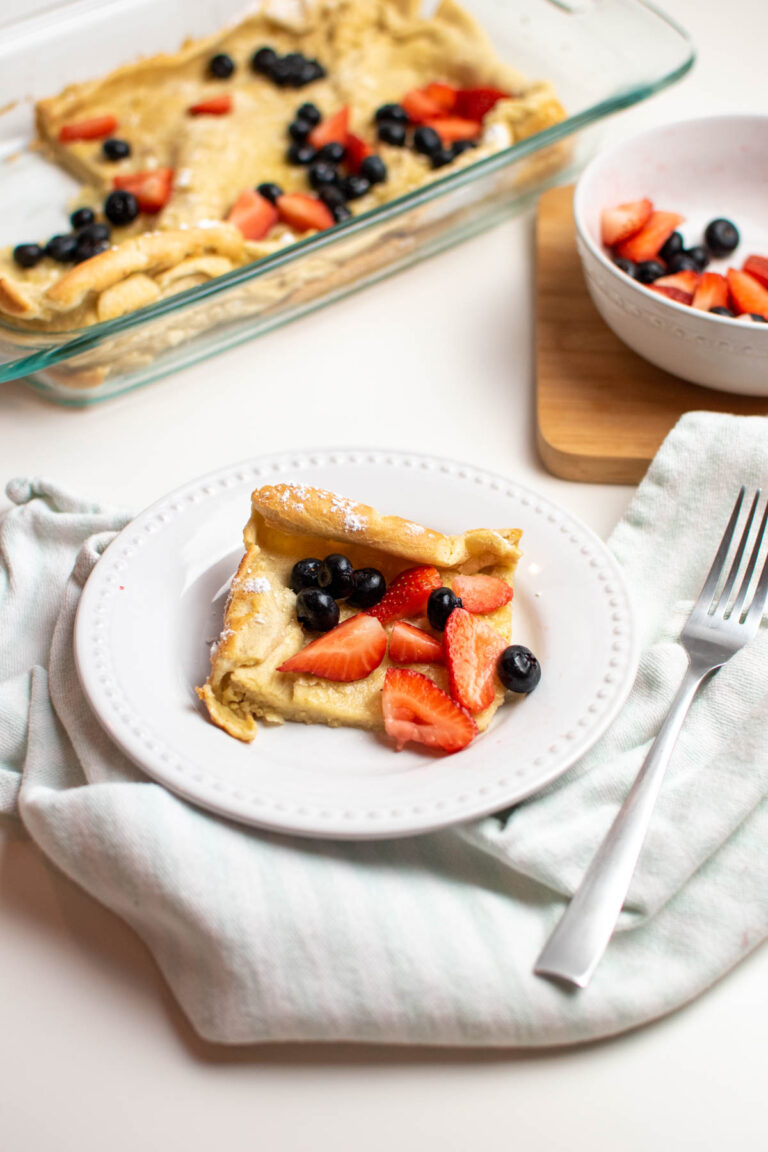 German oven pancakes on white plate next to baking dish filled with pancakes.