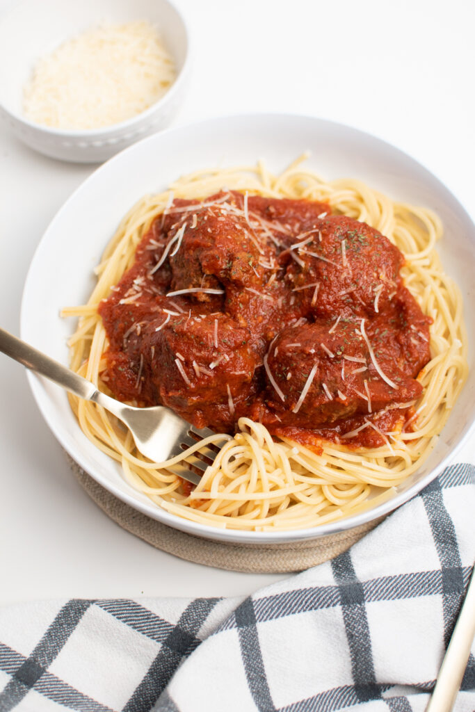 Italian spaghetti and meatballs in a white dish with fork and gray and white kitchen towel.