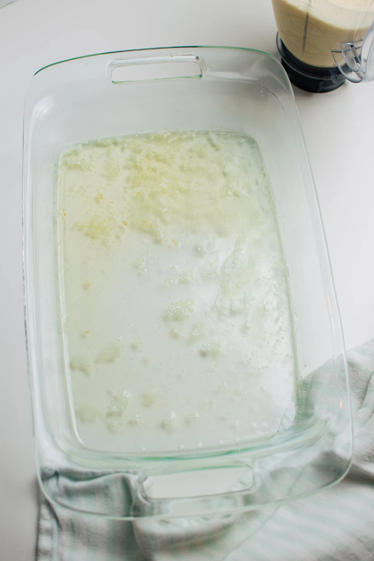 Melted butter in clear glass casserole baking dish with blue and white striped kitchen towel.