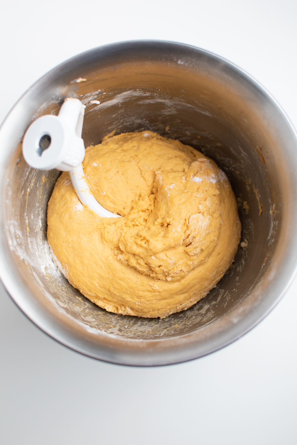 Pumpkin dinner roll dough and a dough hook in large metal bowl.