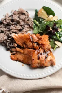 Salmon recipe with brown sugar on white plate with salad and coconut black bean rice.