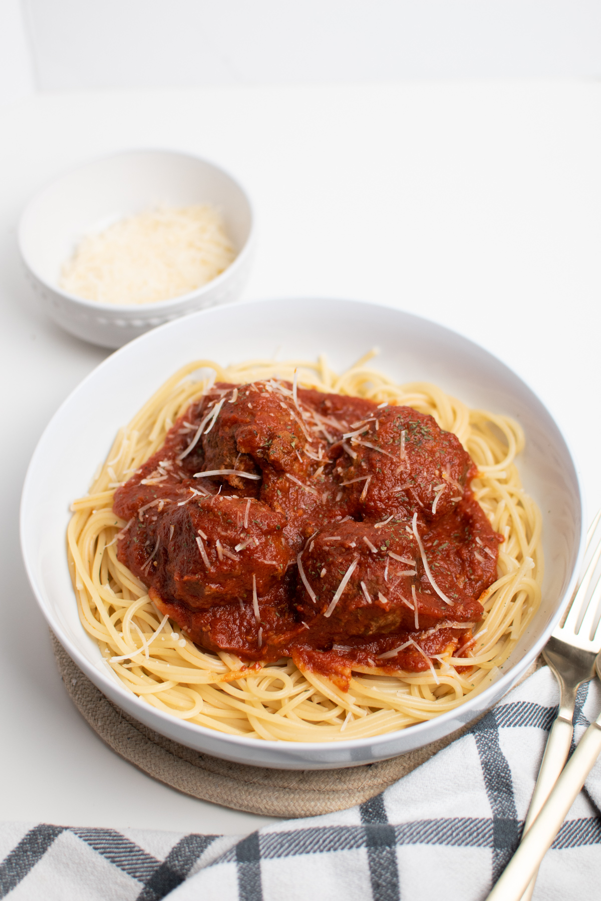 Spaghetti meatball sauce over pasta next to kitchen prep bowl with cheese.