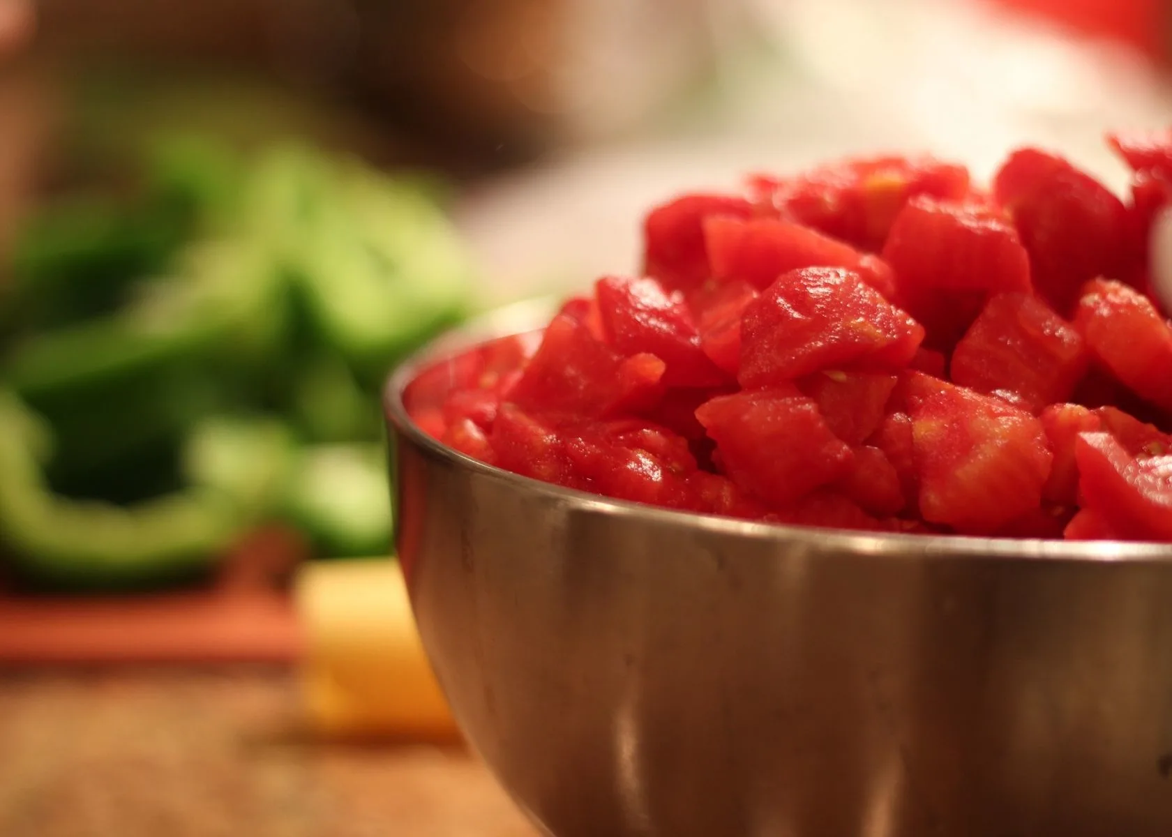 Close up of canned, diced tomatoes in bowl with other ingredients in background.