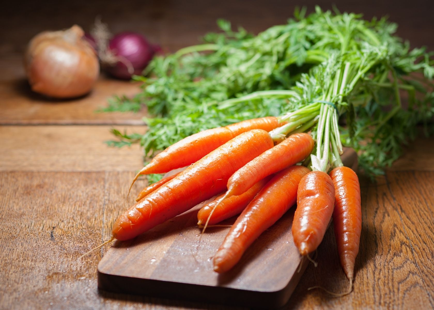 Large bunch of carrots with stems tight together on small wooden cutting board.