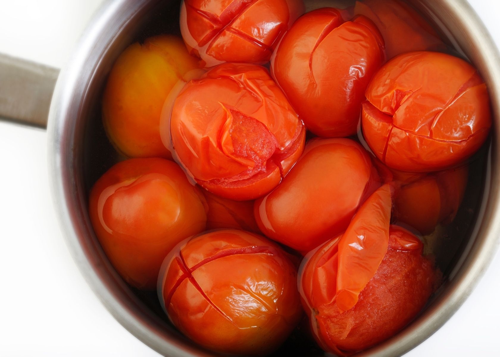 Scored and cooked whole tomatoes in large metal cooking pot filled with water.