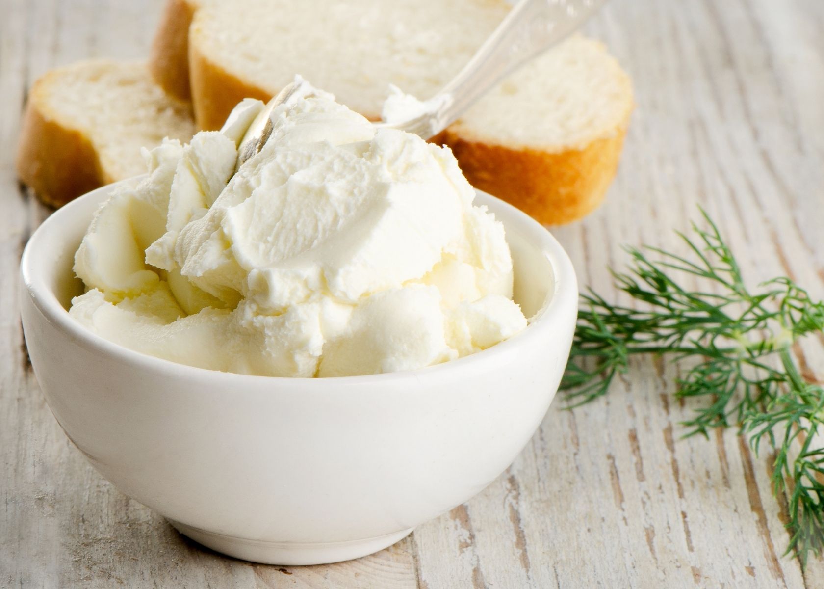 Cream cheese piled high in white bowl next to bread and garnish.