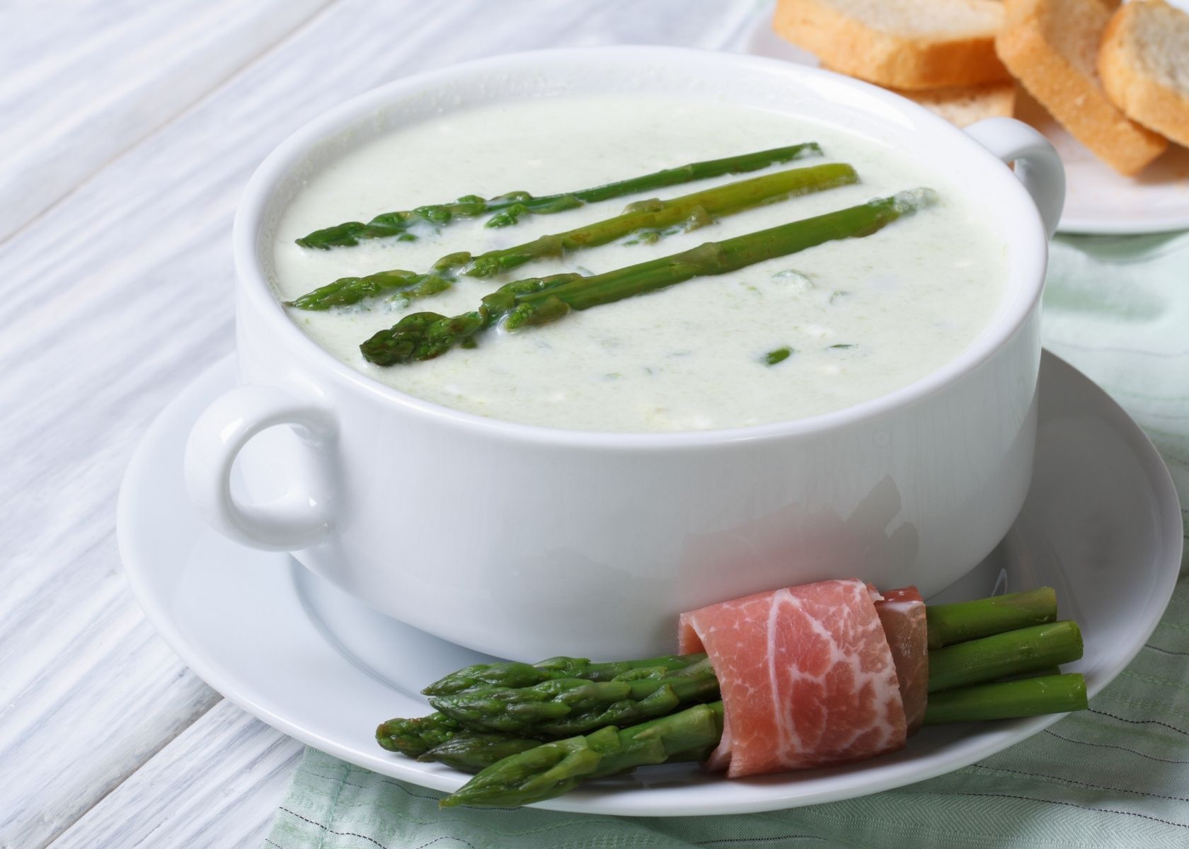 Cream of asparagus soup topped with three asparagus spears in white bowl.