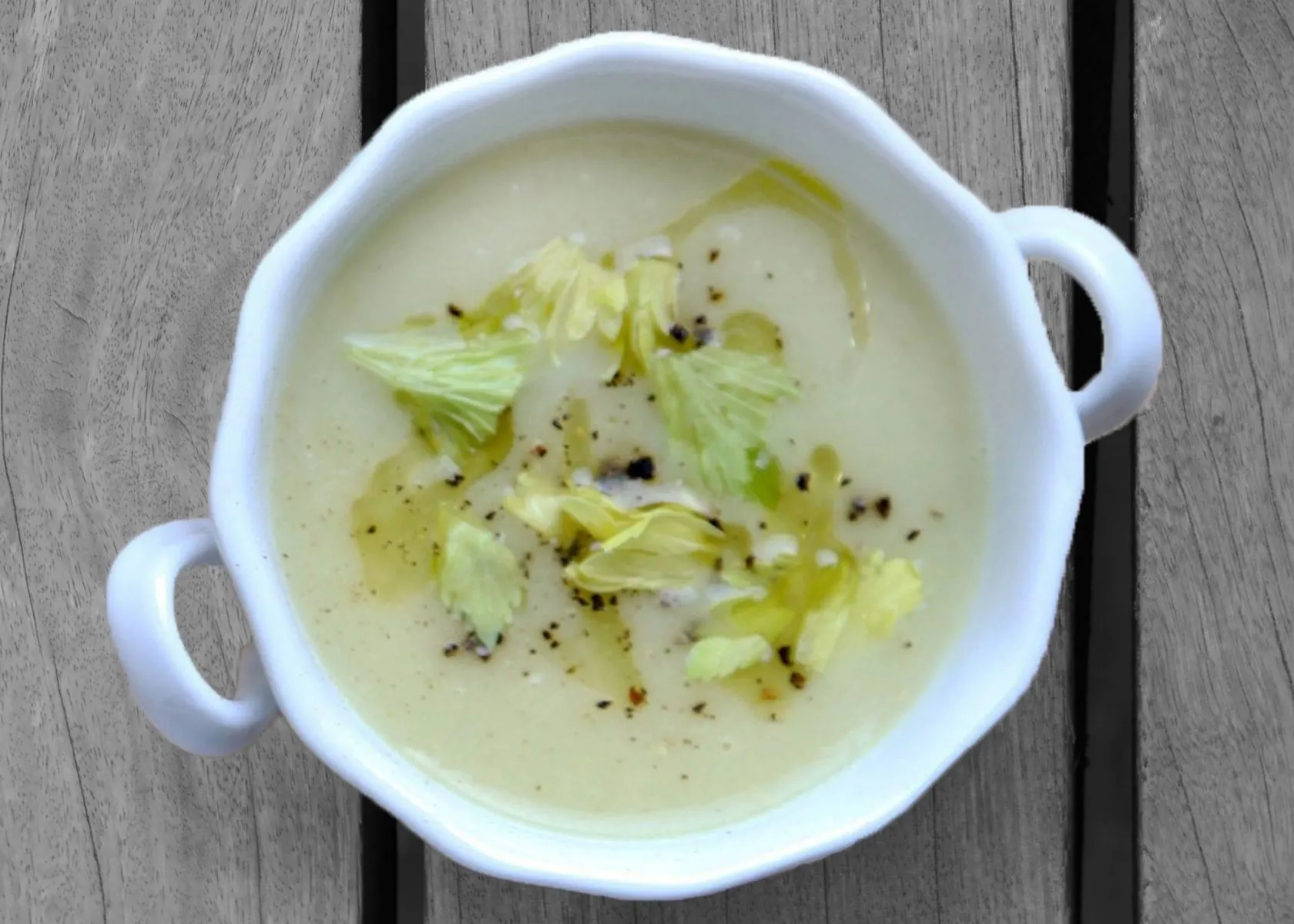 Cream of celery soup in white bowl with celery leaves for garnish.