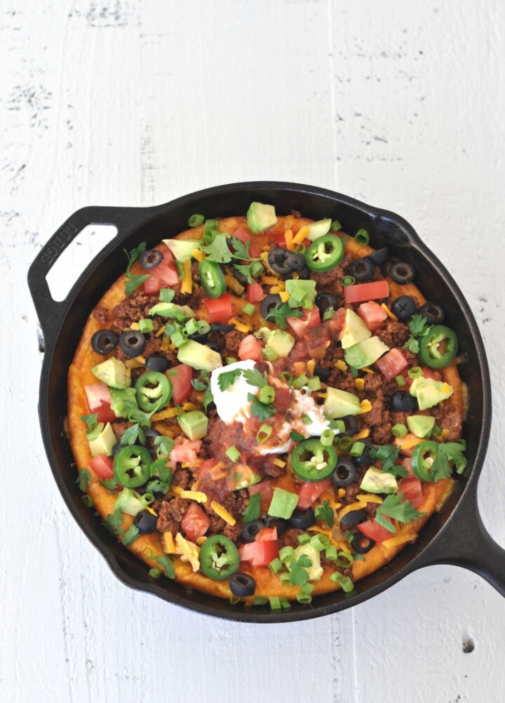 Taco breakfast skillet topped with sour cream, jalapenos and avocado on a white table.