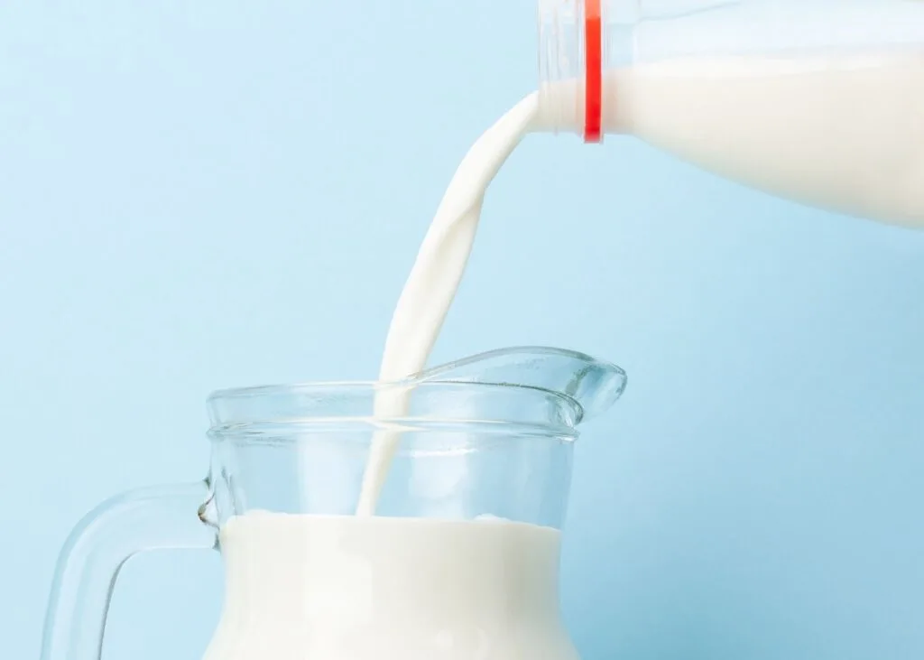 Cow's milk is poured from the jug into a clear glass pitcher.