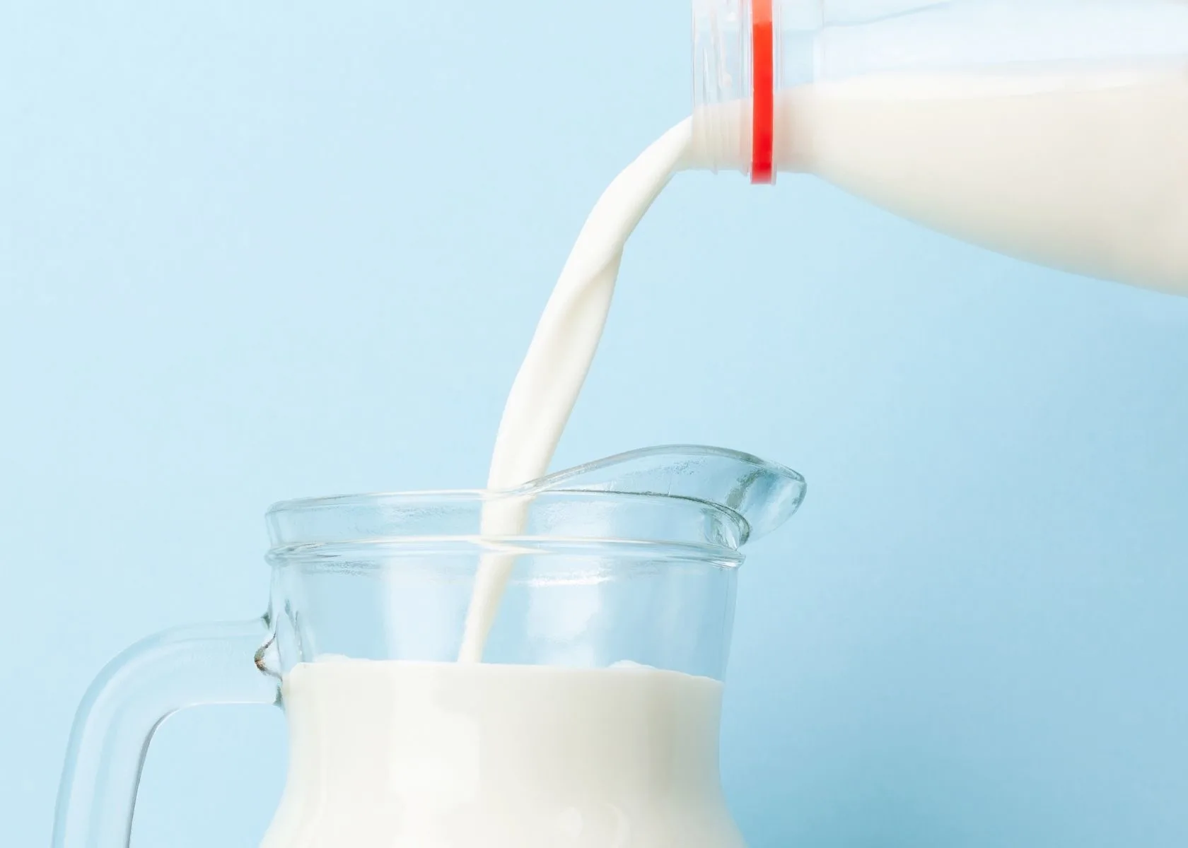 Cow's milk is poured from the jug into a clear glass pitcher.